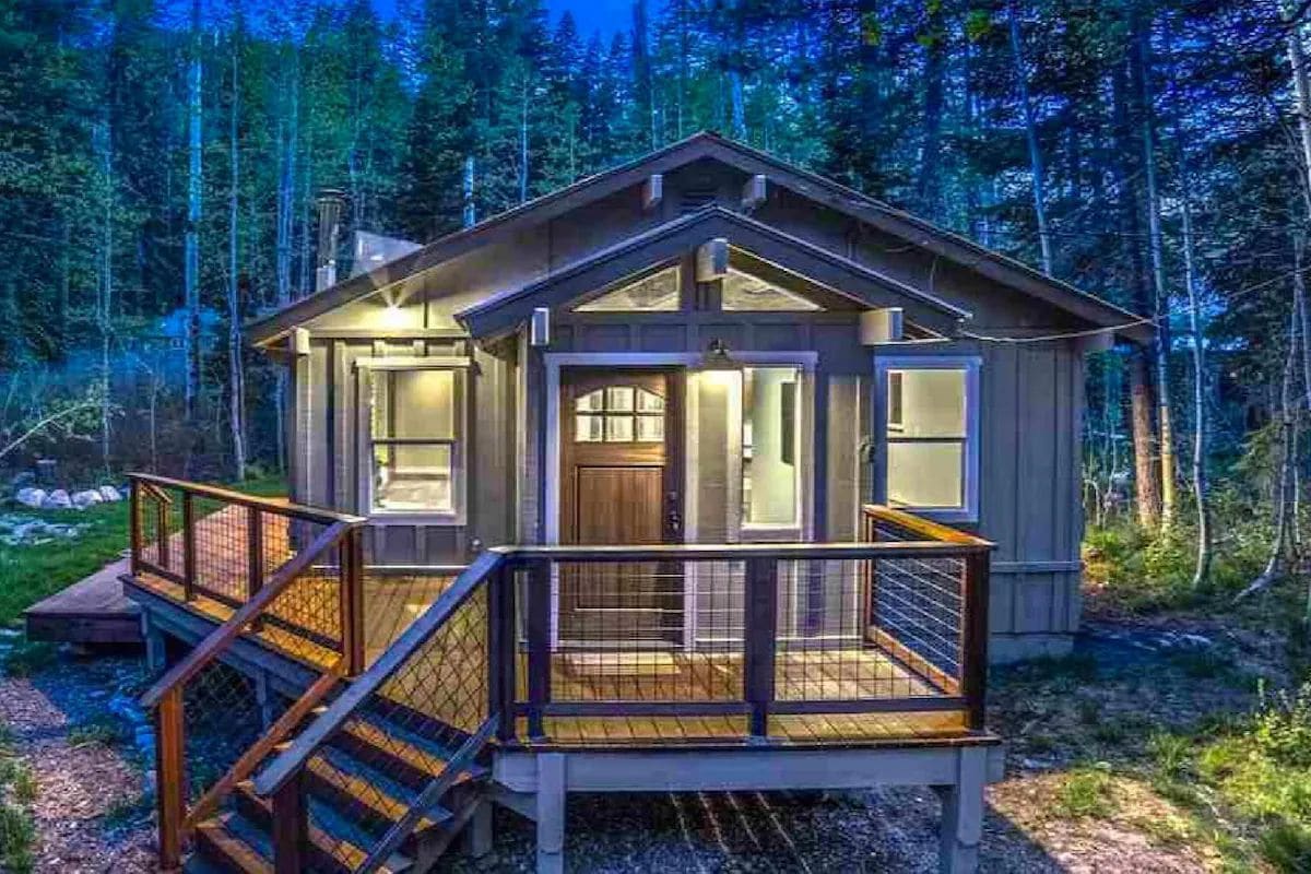A cabin with a wooden deck, a front door, and a staircase leading to the entrance.