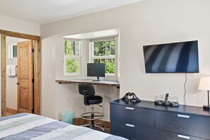 Une chambre à coucher avec un lit, un bureau avec un ordinateur, une chaise, une télévision et une commode.