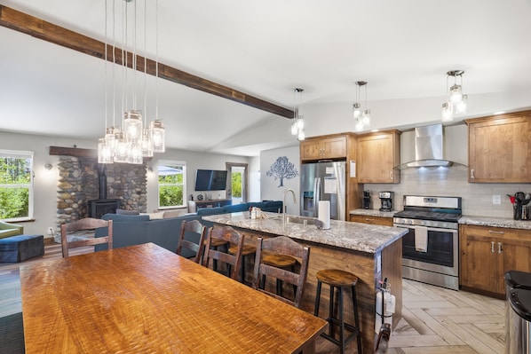 Une cuisine moderne dotée d’un grand îlot central, de meubles en bois, d’appareils électroménagers en acier inoxydable et d’une cheminée en pierre.