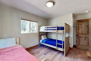 A room with bunk beds, a window, a wooden door, and a bed with a pink blanket. - Homewood Cabin  - Walk to the Lake - Pet Friendly (Homewood)