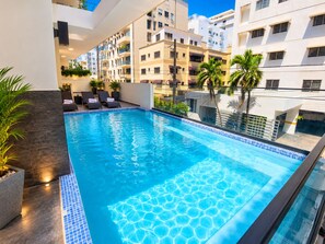 A rooftop swimming pool with lounge chairs and potted plants. - Modern Condo in Evaristo Morales w/Pool & Gym (Santo Domingo)