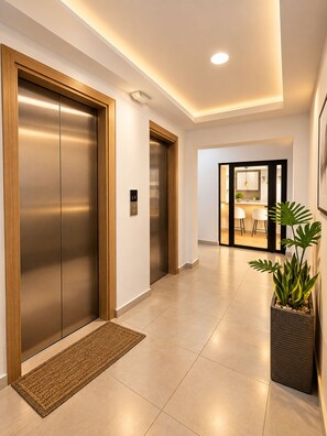 A modern interior with two elevators, a hallway leading to a dining area, and a potted plant. - Modern Condo in Evaristo Morales w/Pool & Gym (Santo Domingo)