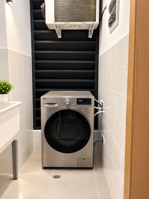 A compact laundry room with a front-loading washing machine, a sink, and a ventilation unit above. - Modern Condo in Evaristo Morales w/Pool & Gym (Santo Domingo)