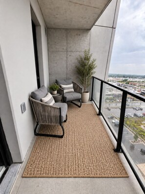 Un balcon avec deux chaises, une petite table et un pot de fleurs.