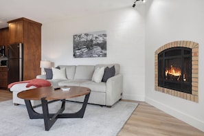 Ein Wohnzimmer mit Kamin, einer Couch, einem Couchtisch und einer Küchenzeile mit Kühlschrank.