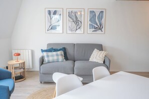 A living room with a grey sofa, white chairs, a small table, and three framed artworks on the wall. - Duplex lumineux avec balcon et parking (Vannes)