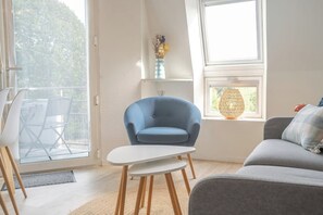 A modern living room with a blue armchair, a grey sofa, and a white coffee table. - Duplex lumineux avec balcon et parking (Vannes)