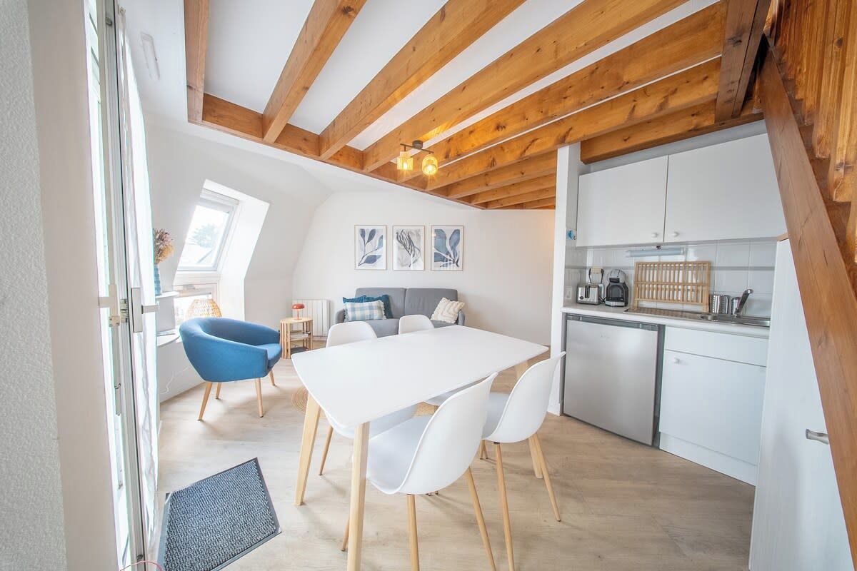 Een moderne keuken met witte kastjes, een eethoek met een witte tafel en stoelen, en een houten plafond.