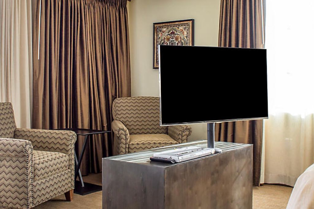 Ein Hotelzimmer mit einem Flachbildfernseher auf einem Standfuß, einer Couch und einem gemusterten Sessel.
