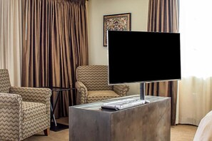 Une chambre d’hôtel équipée d’un téléviseur à écran plat posé sur un meuble, d’un canapé et d’un fauteuil à motifs.