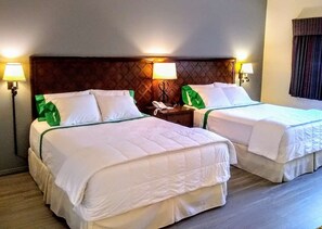 Ein Hotelzimmer mit zwei Betten, jeweils mit weißer Bettwäsche und grünen Akzenten. Auf dem Nachttisch stehen Nachttischlampen und ein Telefon.