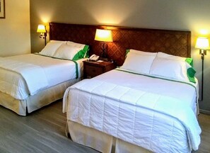 Ein Hotelzimmer mit zwei Betten, jeweils mit weißer Bettwäsche und grünen Akzenten, einem Holz-Kopfteil, Nachttischlampen und einem Nachttisch mit Telefon.