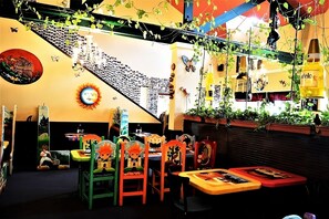 Ein Restaurantinneres mit einer Treppe, Tischen, Stühlen und hängenden Pflanzen.