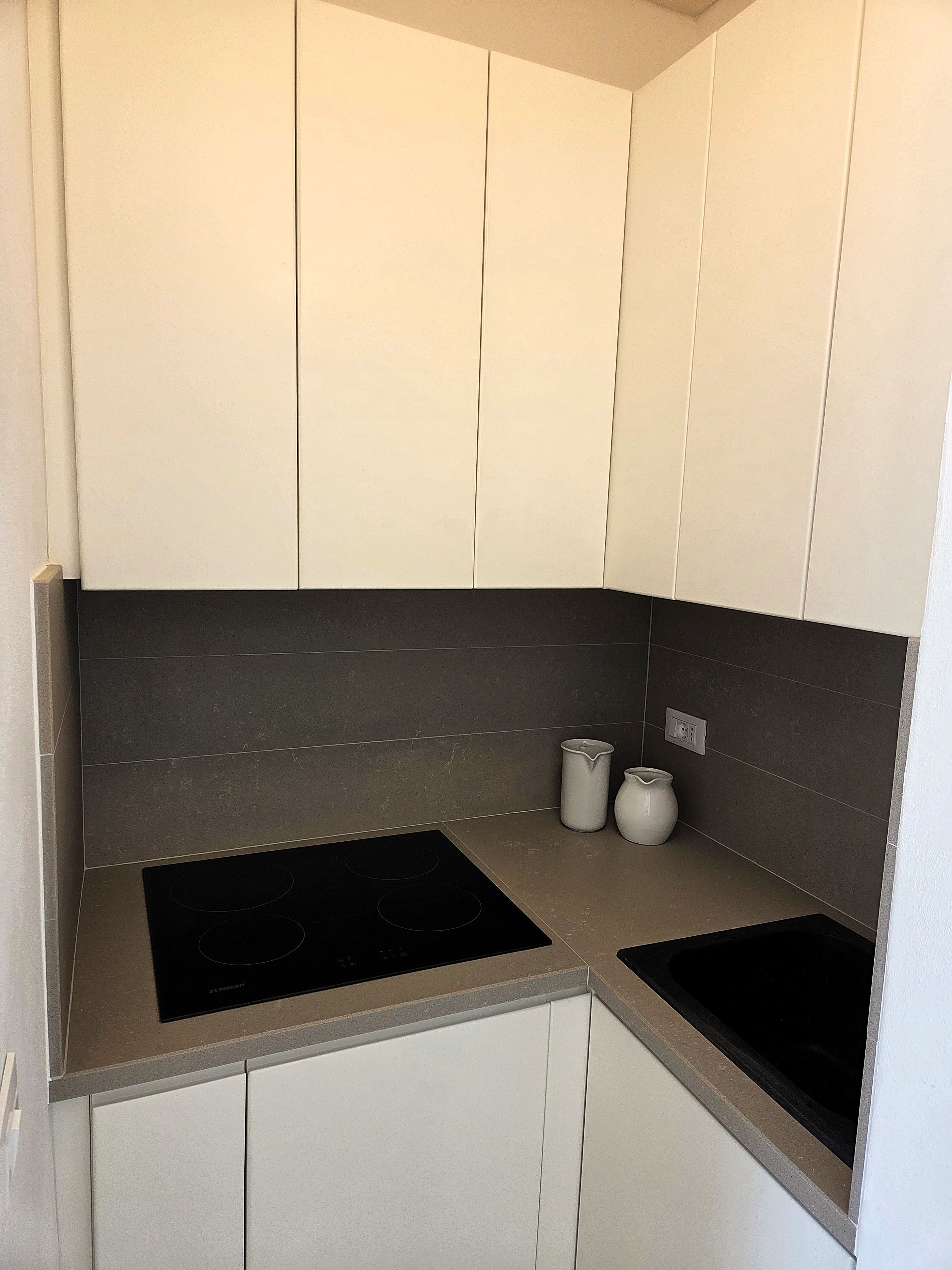A modern kitchen with white cabinets, dark backsplash, and two black induction cooktops.