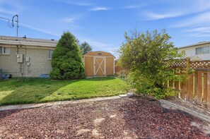 A residential backyard with a lawn, a wooden shed, and a tall coniferous tree. - Spacious Taylorsville Home w Finished Basement! (Taylorsville)
