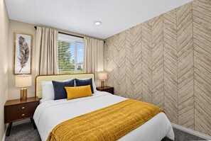 Une chambre d’hôtel avec un lit, des tables de chevet, une lampe, une œuvre d’art en plumes et une fenêtre avec des rideaux.