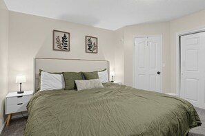 A bedroom with a bed, nightstands, a door, and two wall-mounted pictures. - Spacious Taylorsville Home w Finished Basement! (Taylorsville)