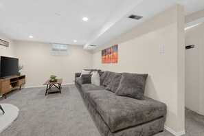 Un salon avec un canapé gris, un téléviseur posé sur un meuble en bois et une petite table sur laquelle se trouve une plante.