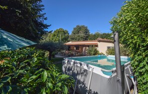 A swimming pool with a covered area, surrounded by lush greenery and a house with a tiled roof in the background. - Lovely home in Campagnano with private swimming pool, can be inside or outside (Campagnano)