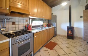 A kitchen with wooden cabinets, a gas stove, a built-in oven, a sink, and a wood-burning stove. - Lovely home in Campagnano with private swimming pool, can be inside or outside (Campagnano)