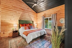 Ein Schlafzimmer einer Holzhütte mit Bett, Nachttisch und Fenster mit Vorhängen.