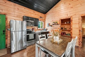 Innenansicht einer Holzhütte mit Küchenbereich, inklusive Kühlschrank, Herd und Mikrowelle.