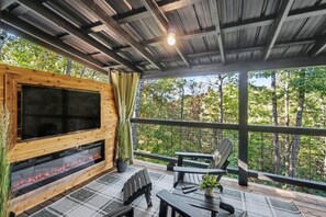 Eine Terrasse im Freien mit eingebautem Kamin, Sitzgelegenheiten und Blick auf den Wald.