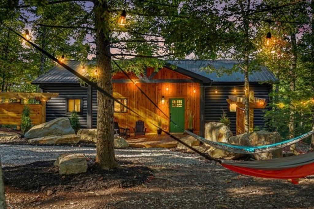 A rustic cabin with a wooden exterior, a green door, and a hammock in the foreground.