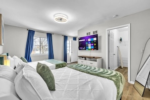 A hotel room with two beds, a flat-screen TV, a wardrobe, and a door leading to another room. - 4BR Family Home • Ideal for Insurance & Work Stays (Lake in the Hills)