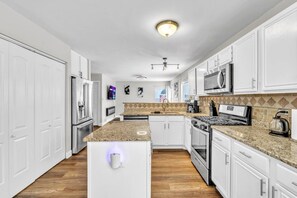 A modern kitchen with white cabinetry, granite countertops, a built-in oven, and a coffee maker. - 4BR Family Home • Ideal for Insurance & Work Stays (Lake in the Hills)
