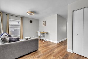 A modern living room with a grey sofa, a small white table, and a wooden floor. - 4BR Family Home • Ideal for Insurance & Work Stays (Lake in the Hills)