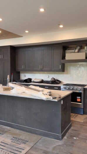 A kitchen with dark cabinets, a central island, and a stove. - Luxury Meets Location | Hot Tub and Firepit (Canmore)