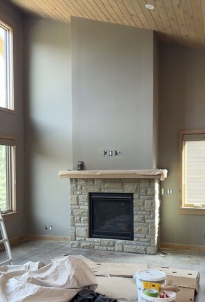 A room with a stone fireplace, a wooden ceiling, and large windows. - Luxury Meets Location | Hot Tub and Firepit (Canmore)