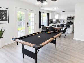 Mesa de bilhar numa cozinha moderna, com área de refeições e vista para o exterior.