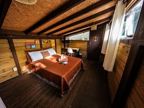 A wooden cabin bedroom with a bed, a desk, and a window. - Cabana Caapora: tranquilidade em meio à natureza em Florianópolis (Florianópolis)