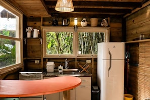 A compact kitchen with a refrigerator, a sink, and a window with a view of bamboo. - Cabana Caapora: tranquilidade em meio à natureza em Florianópolis (Florianópolis)