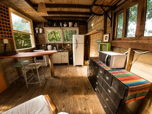 A compact kitchen with a refrigerator, microwave, and a small dining area with stools.