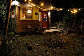 A rustic wooden cabin with a porch, a red door, and string lights.