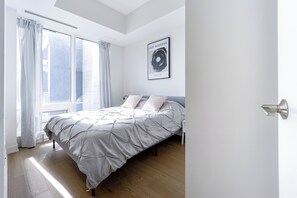 A bedroom with a bed, curtains, a framed artwork, and a door. - Modern Downtown Montreal 1-Bedroom Condo with Pool & Rooftop (Montréal)
