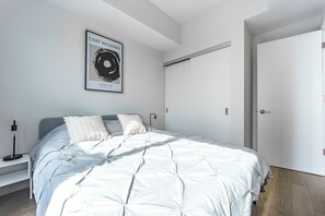 A modern bedroom with a bed, bedside tables, a framed artwork, and a wardrobe. - Modern Downtown Montreal 1-Bedroom Condo with Pool & Rooftop (Montréal)