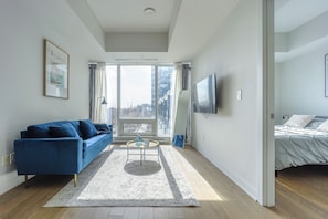 A modern living room with a blue sofa, a coffee table, and a large window. - Modern Downtown Montreal 1-Bedroom Condo with Pool & Rooftop (Montréal)