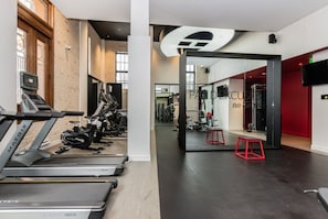 A gym with treadmills, weight machines, and a red accent wall. - Modern Downtown Montreal 1-Bedroom Condo with Pool & Rooftop (Montréal)
