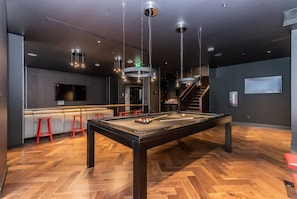 A pool table in a modern room with a herringbone wood floor, a bar area with stools, and a staircase. - Modern Downtown Montreal 1-Bedroom Condo with Pool & Rooftop (Montréal)