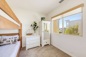 A bedroom with a bed, a dresser, a mirror, and a window with a view of buildings and trees. - La Jolla Beach House -  Walk to Windansea, EV Charger (San Diego)