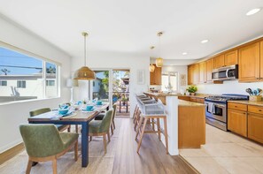 A modern kitchen with wooden cabinets, a stainless steel oven, and a dining area with a table set for four. - La Jolla Beach House -  Walk to Windansea, EV Charger (San Diego)