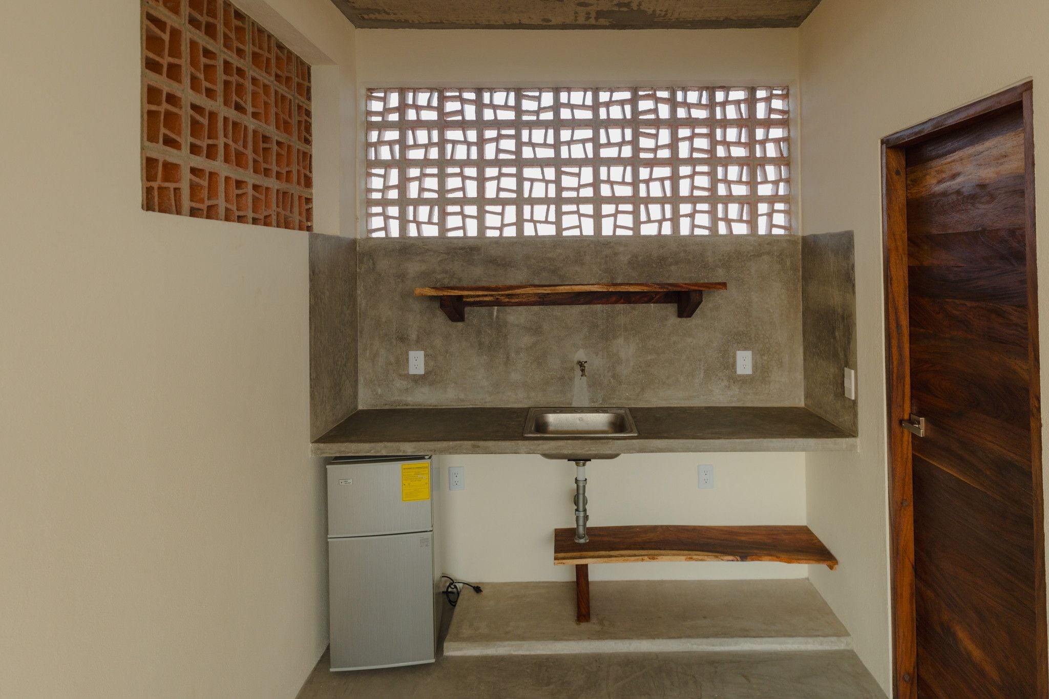 A compact kitchen with a built-in sink, a small refrigerator, and a wooden door.