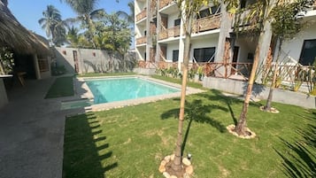 Un patio de hotel con piscina, palmeras y una estructura de techo de paja.