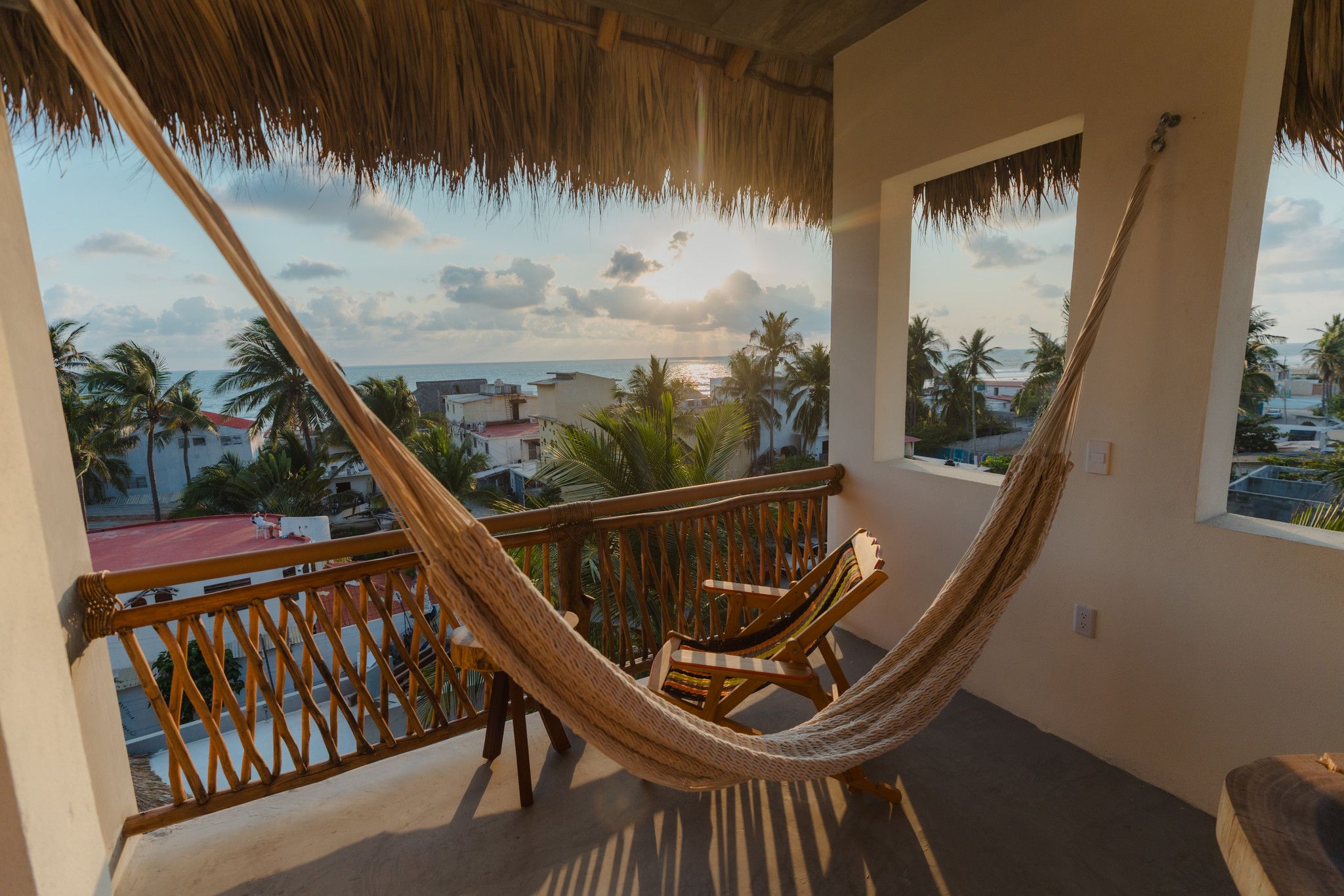 Una hamaca en un balcón con vista a la costa, edificios y palmeras.