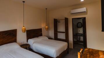 Ein Hotelzimmer mit zwei Betten, einem Holz-Kopfteil, einem kleinen Nachttisch, einer Pendelleuchte und einer Klimaanlage.