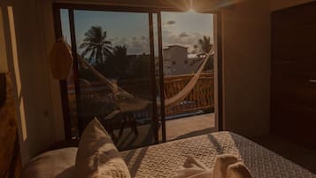 Un dormitorio con cama, hamaca y vistas a palmeras y edificios a través de una puerta corredera.